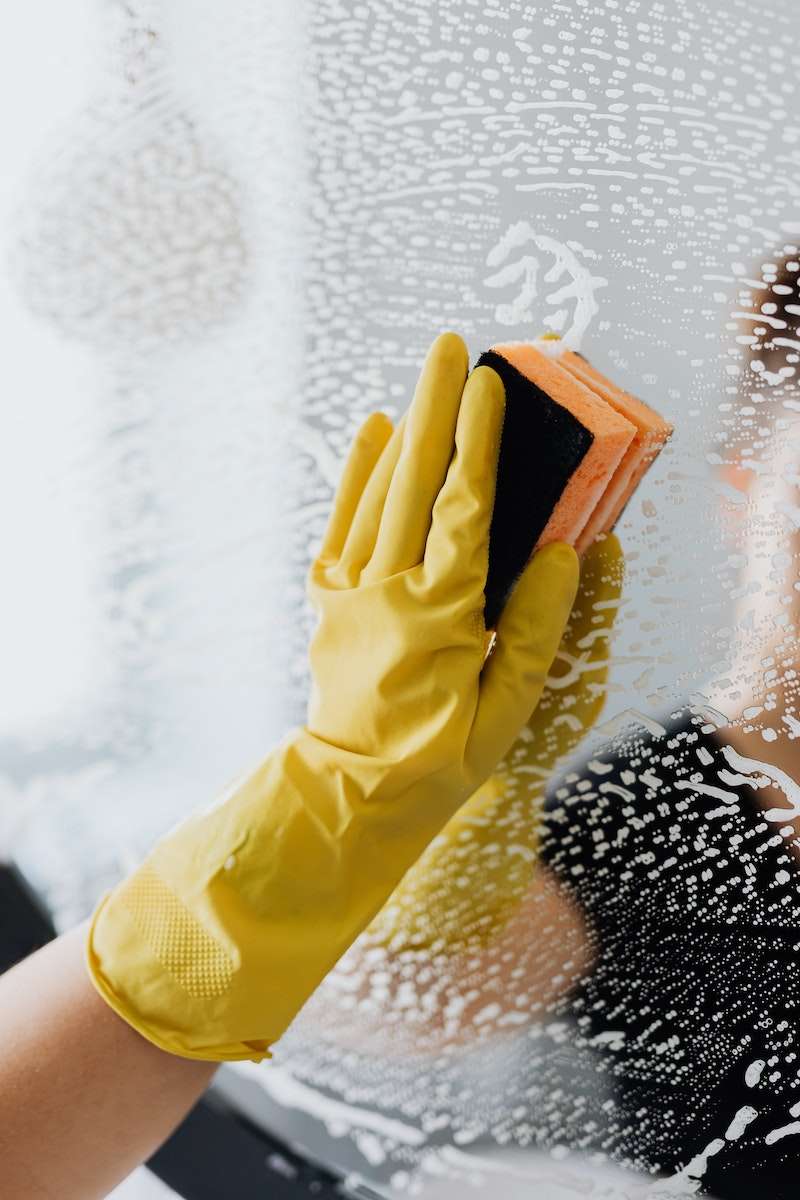 Housekeeper in yellow rubber gloves cleaning mirror with sponge
